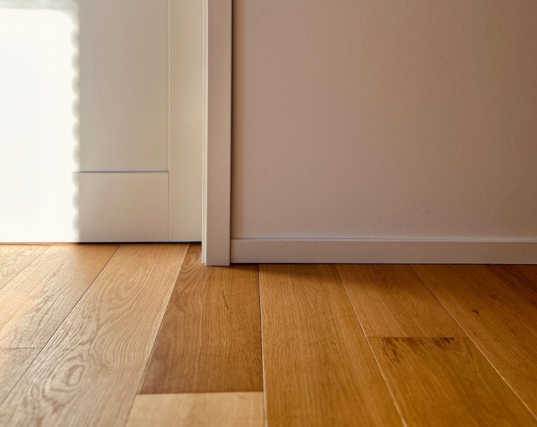 Detail eines hellen Parkettbodens mit Sockelleiste und Wandanschluss im Innenraum