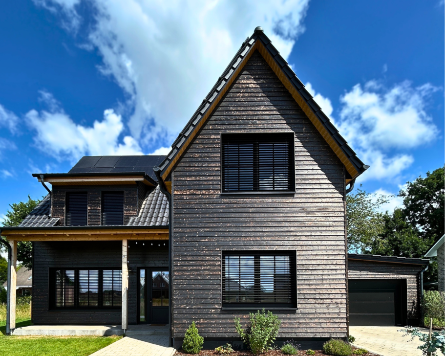 Frontansicht eines Einfamilienhauses mit geflammter, karbonisierter Holzfassade (Carboris), modernen Fenstern und Garage
